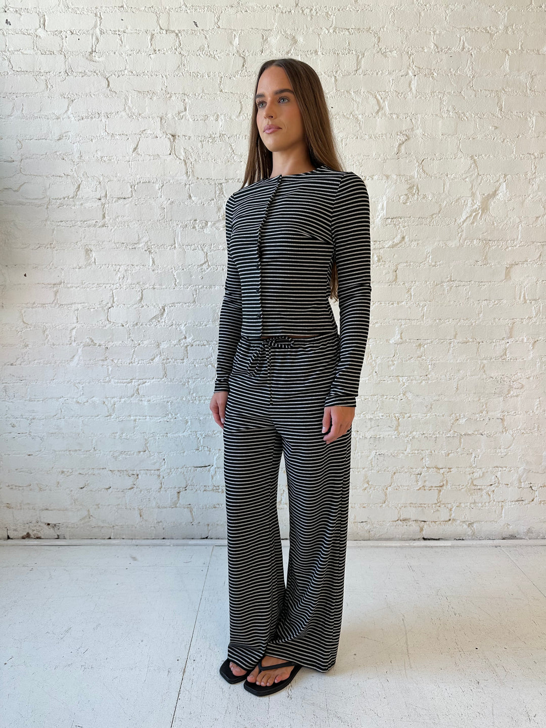 Woman wearing black striped two piece lounge set with button down long sleeve top.