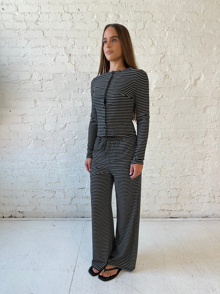 Woman wearing black striped two piece lounge set with button down long sleeve top.