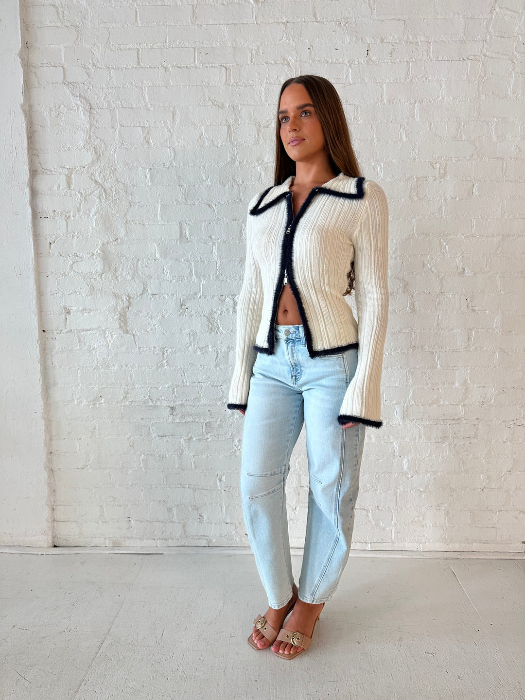 Woman wearing ivory knit long sleeve top with double zipper closure, and light wash barrel jeans.