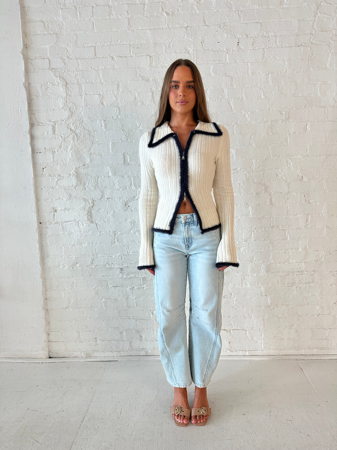 Woman wearing ivory knit long sleeve top with double zipper closure, and light wash barrel jeans.