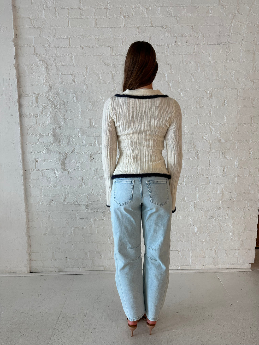 Woman wearing ivory knit long sleeve top with double zipper closure, and light wash barrel jeans.