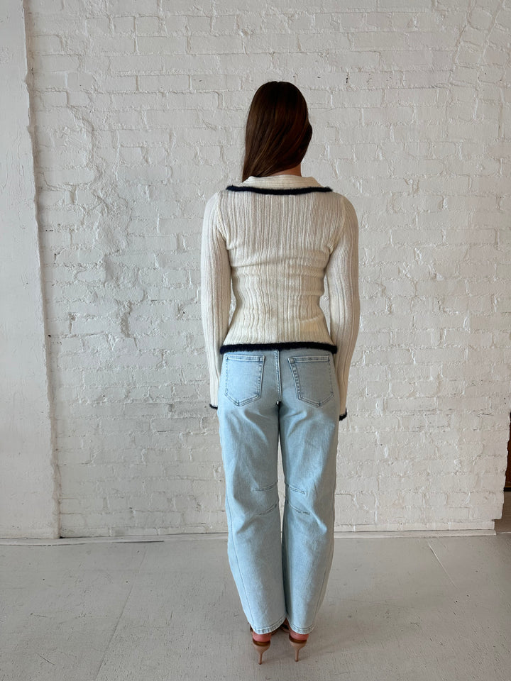 Woman wearing ivory knit long sleeve top with double zipper closure, and light wash barrel jeans.