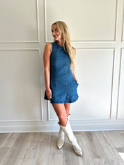 Woman wearing a dark wash denim mini dress with functional pockets.