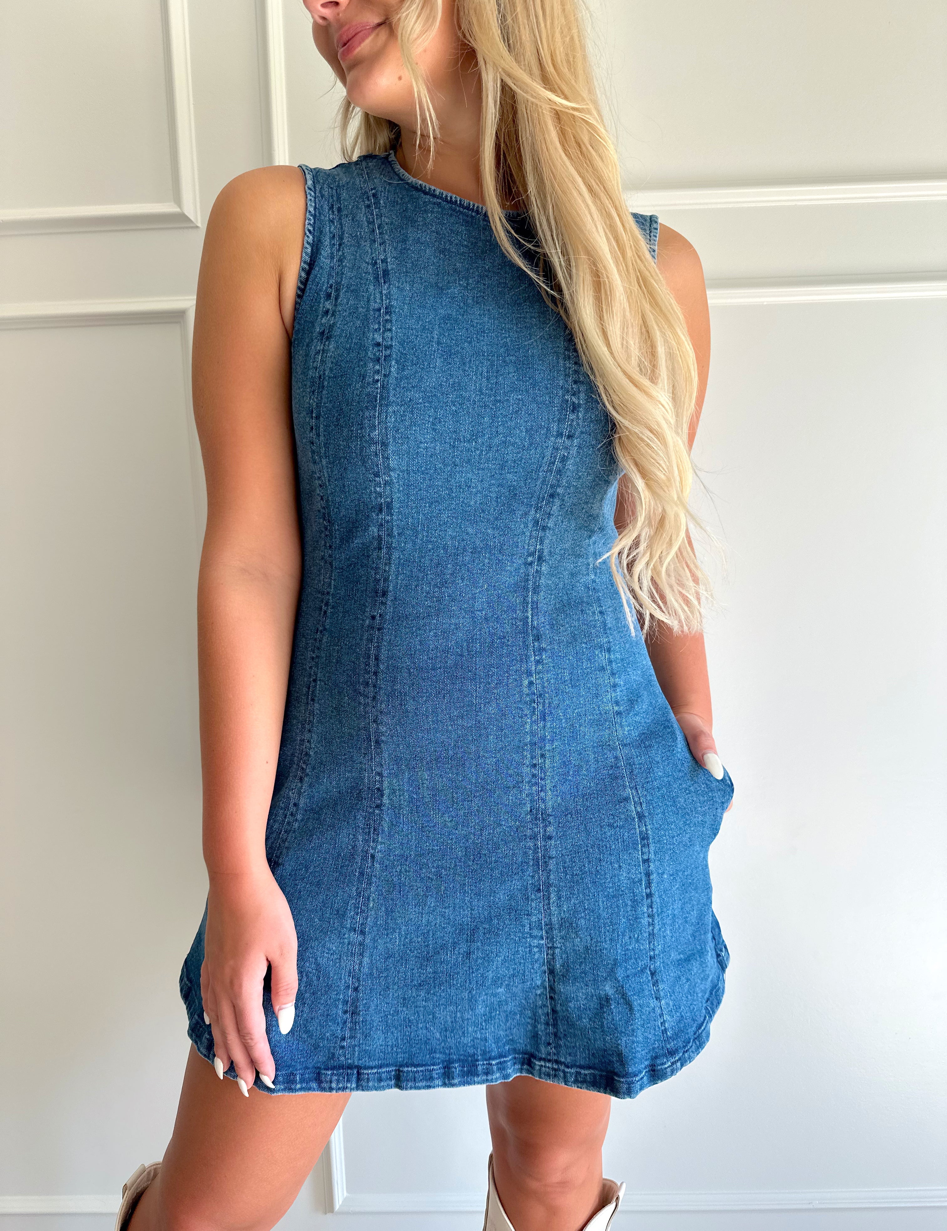 Woman wearing a dark wash denim mini dress with functional pockets.