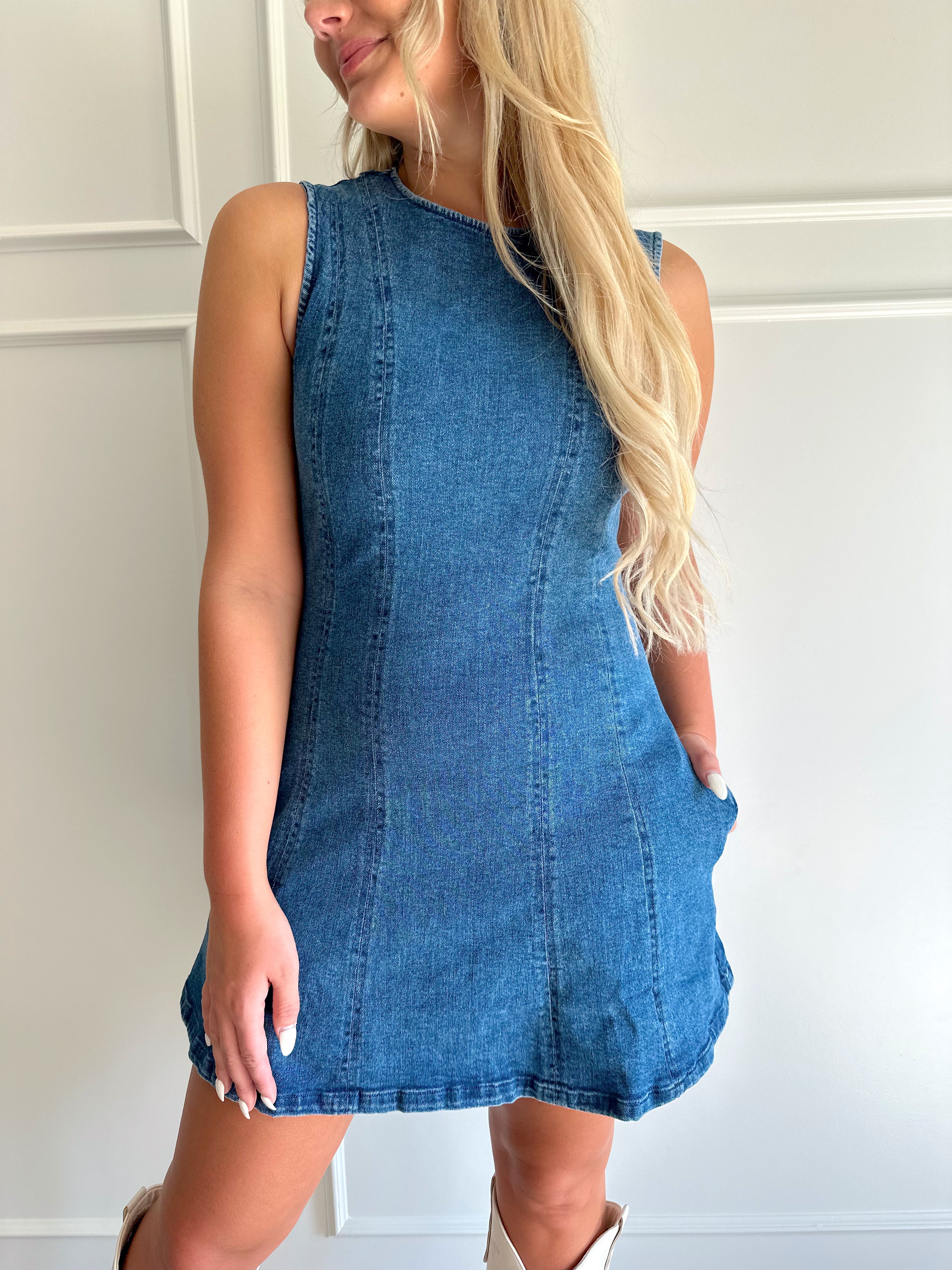Woman wearing a dark wash denim mini dress with functional pockets.