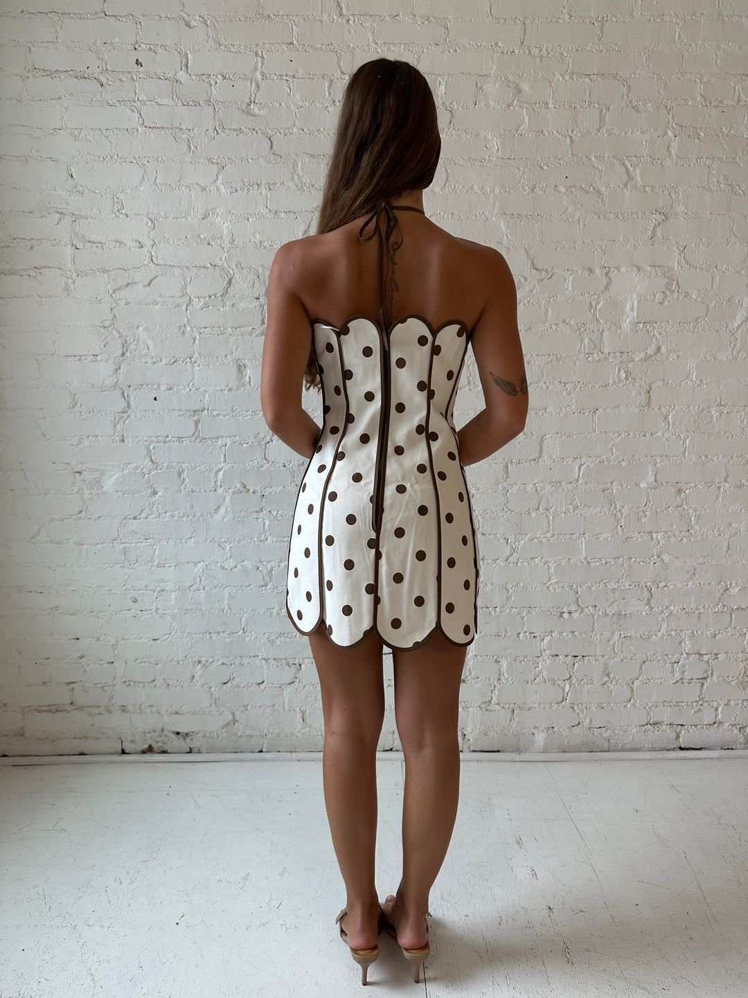Woman wearing cream and brown polka dot mini dress with scallop neckline and hem.