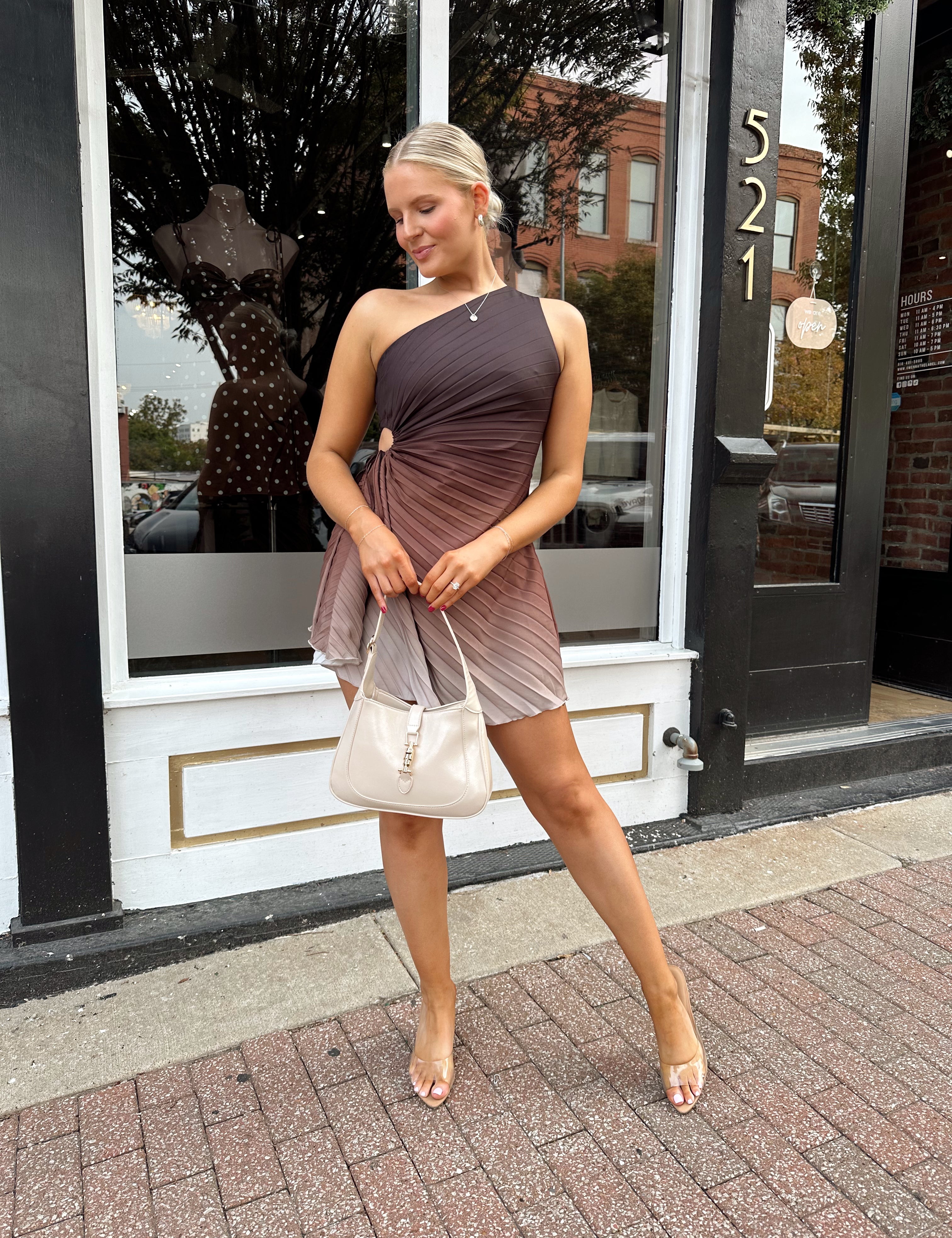 Woman wearing one shoulder brown ombré pleated mini dress with adjustable side cutout. 