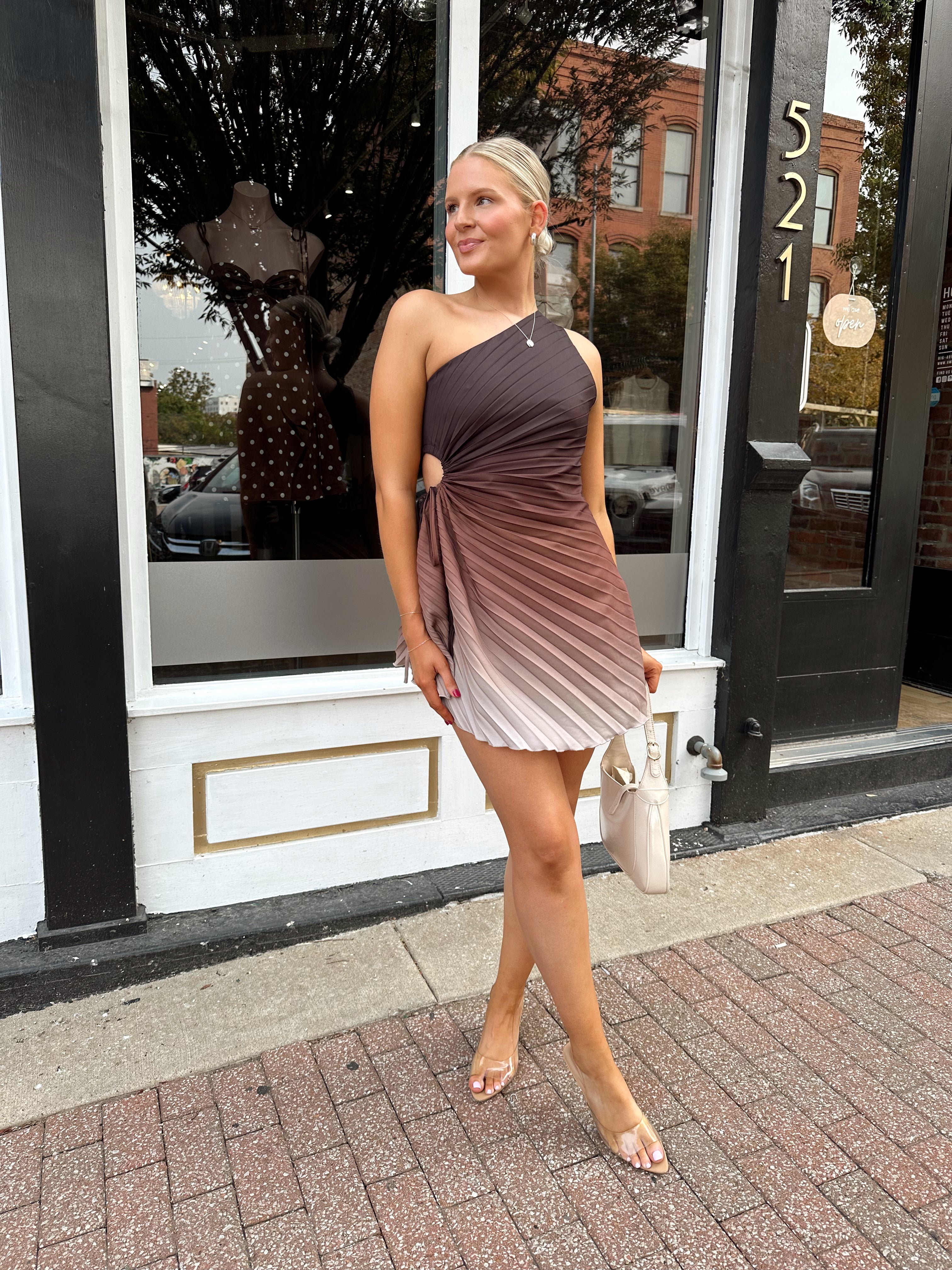 Woman wearing one shoulder brown ombré pleated mini dress with adjustable side cutout. 