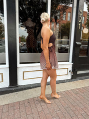 Woman wearing one shoulder brown ombré pleated mini dress with adjustable side cutout. 