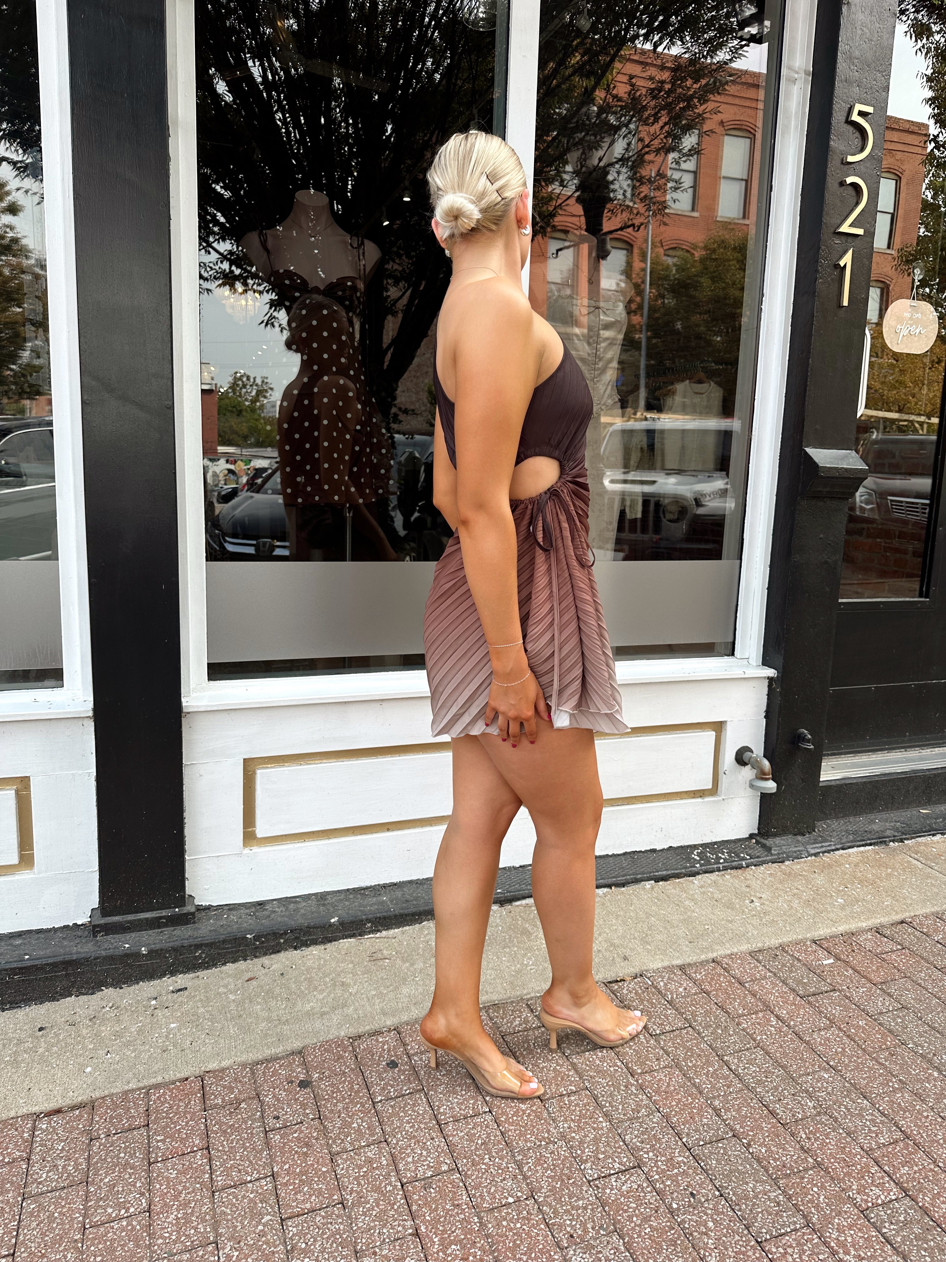 Woman wearing one shoulder brown ombré pleated mini dress with adjustable side cutout. 