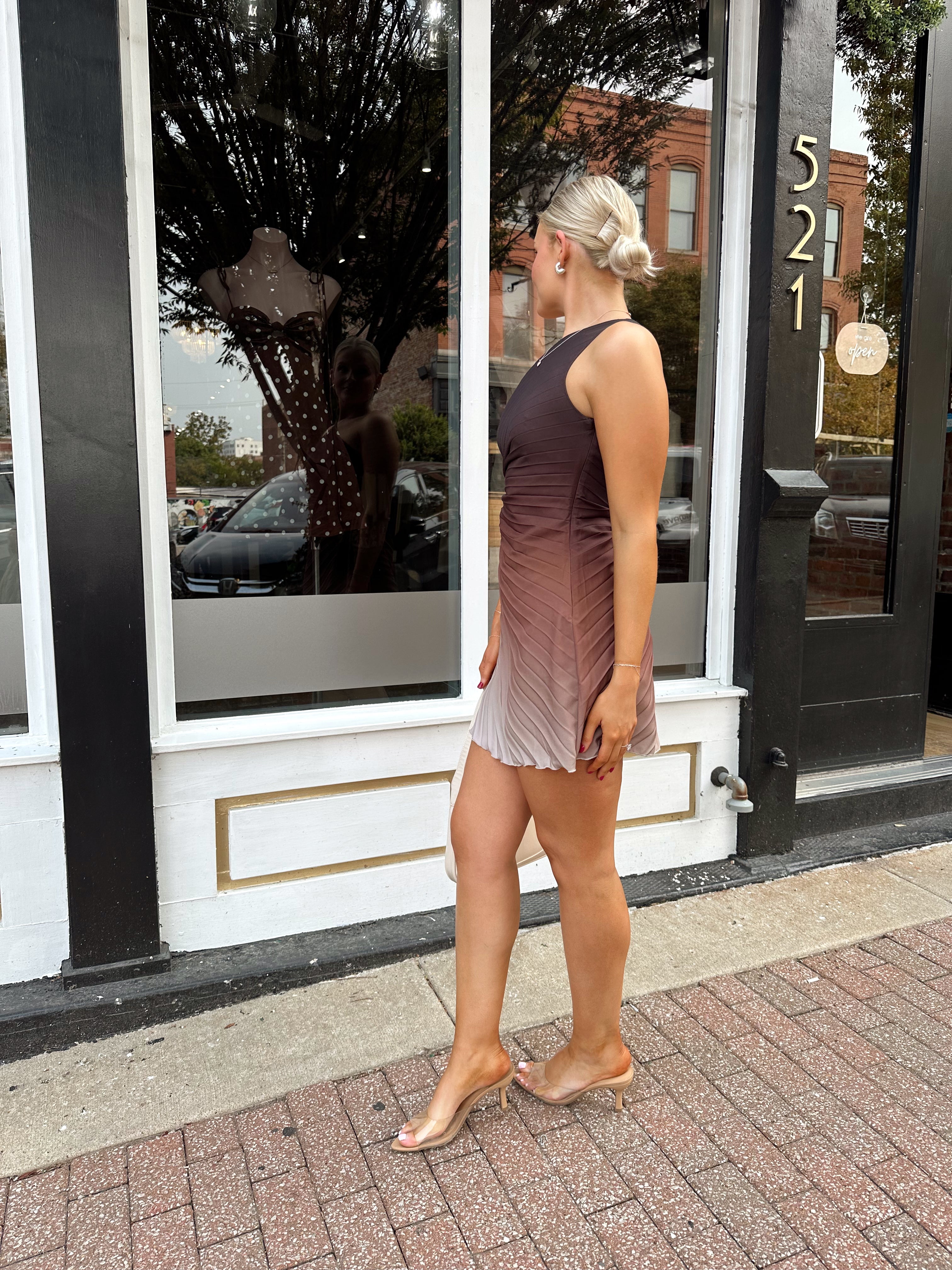 Woman wearing one shoulder brown ombré pleated mini dress with adjustable side cutout. 