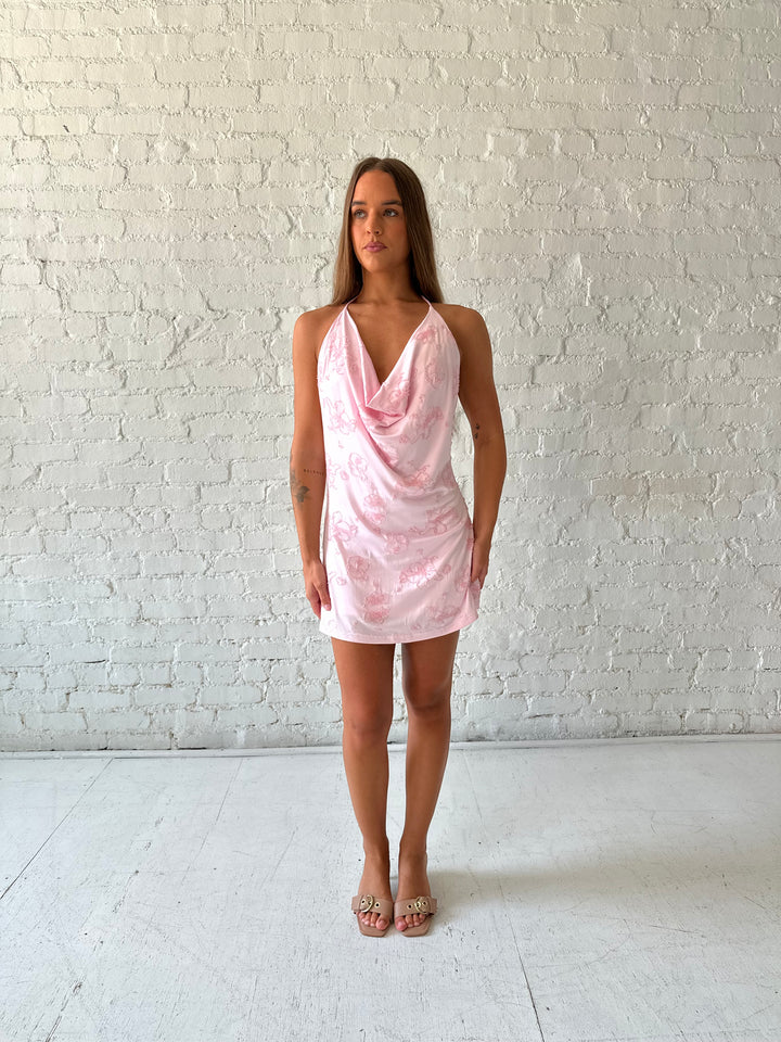 Woman wearing light pink mini dress with beaded embellished detailing and cowl, halter neckline. 