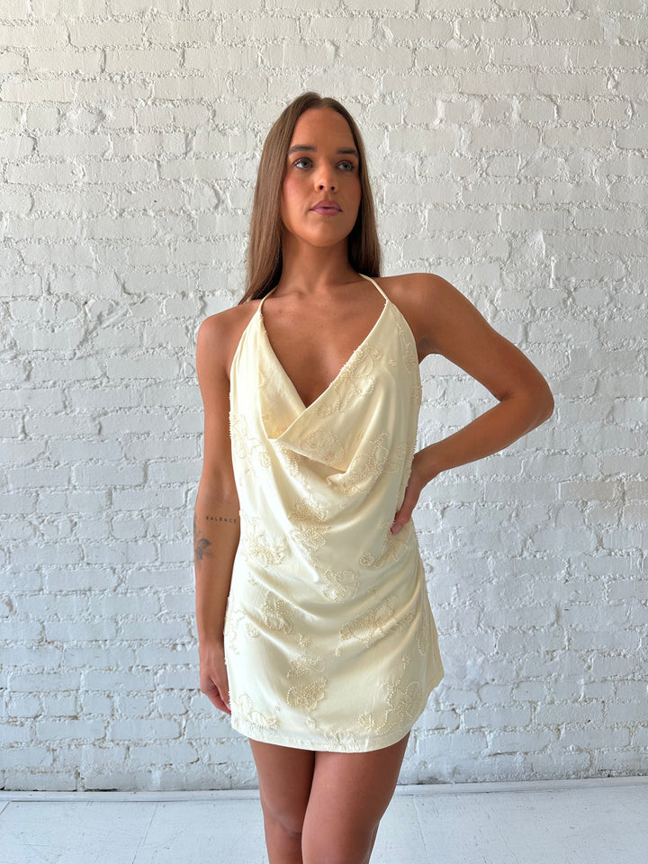 Woman wearing yellow halter beaded mini dress with cowl neckline and low back.