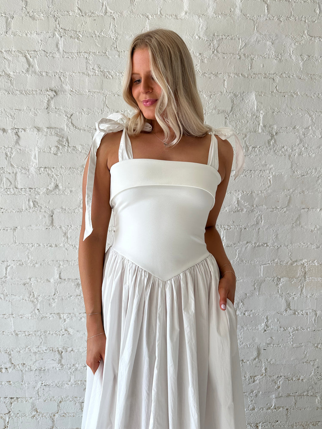 Woman wearing white maxi dress with tie strap detailing, and fold over neckline. 