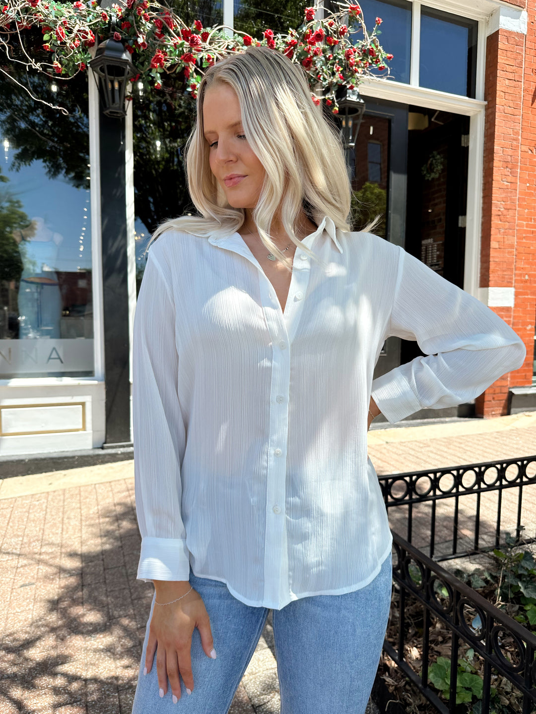 Woman wearing white textured button down top with distress jean. 