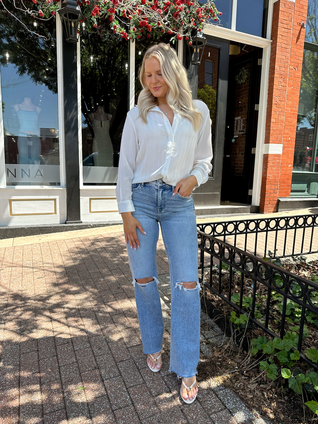 Woman wearing white textured button down top with distress jean. 