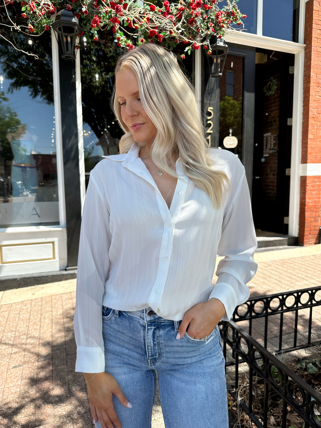 Woman wearing white textured button down top with distress jean. 