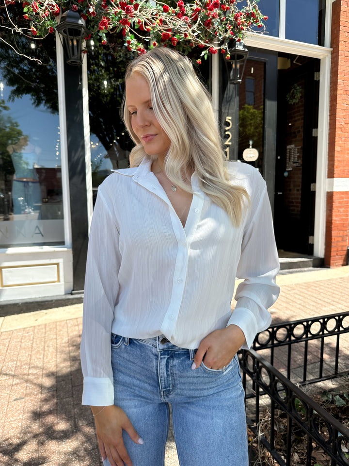 Woman wearing white textured button down top with distress jean. 