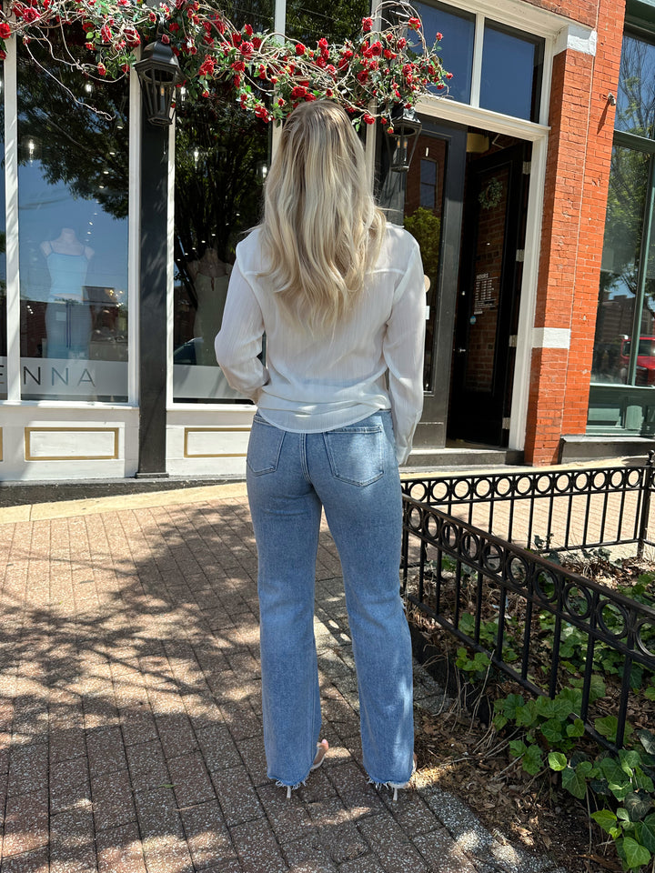 Woman wearing white textured button down top with distress jean. 