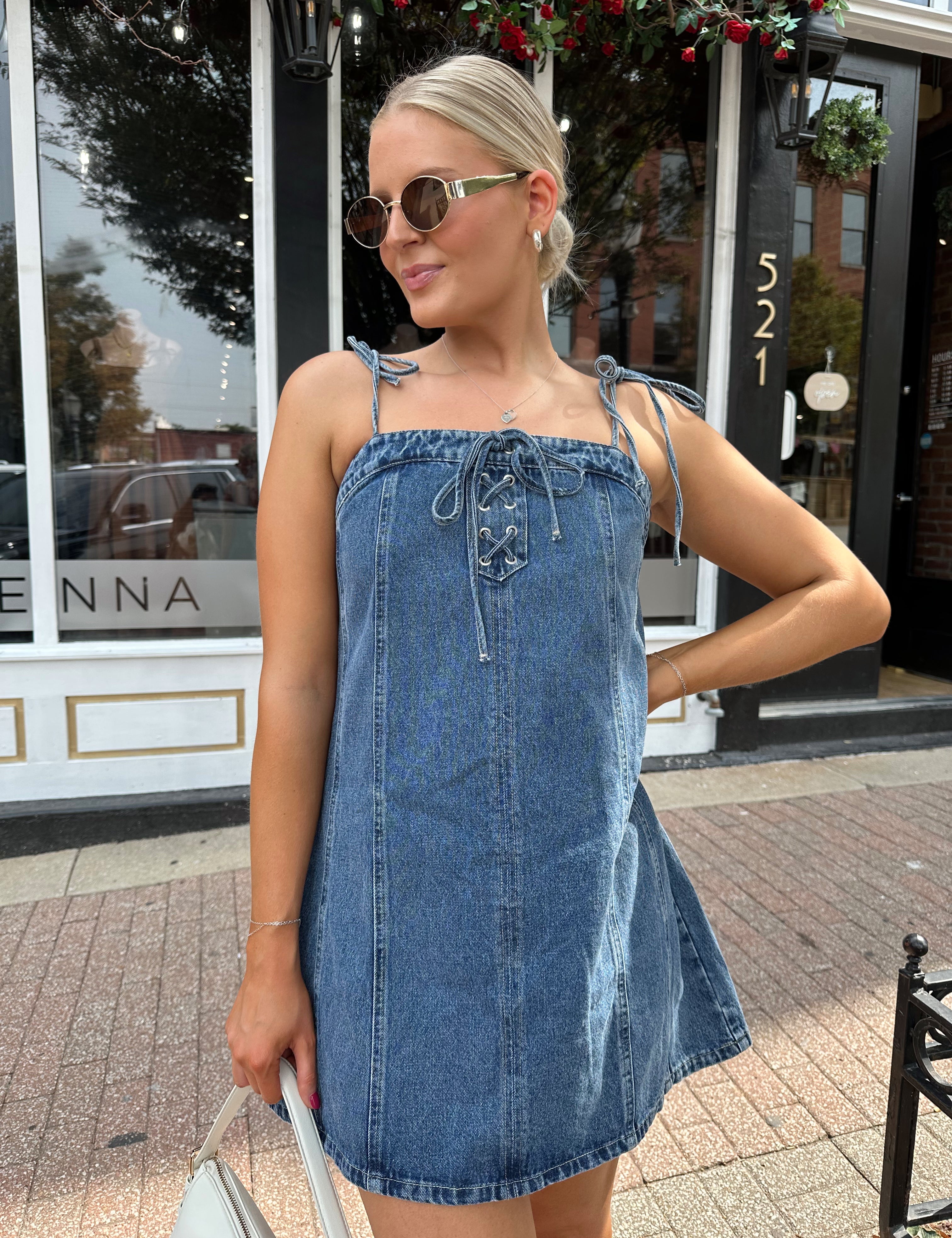 Woman wearing dark wash denim mini dress with lace up neckline detail.