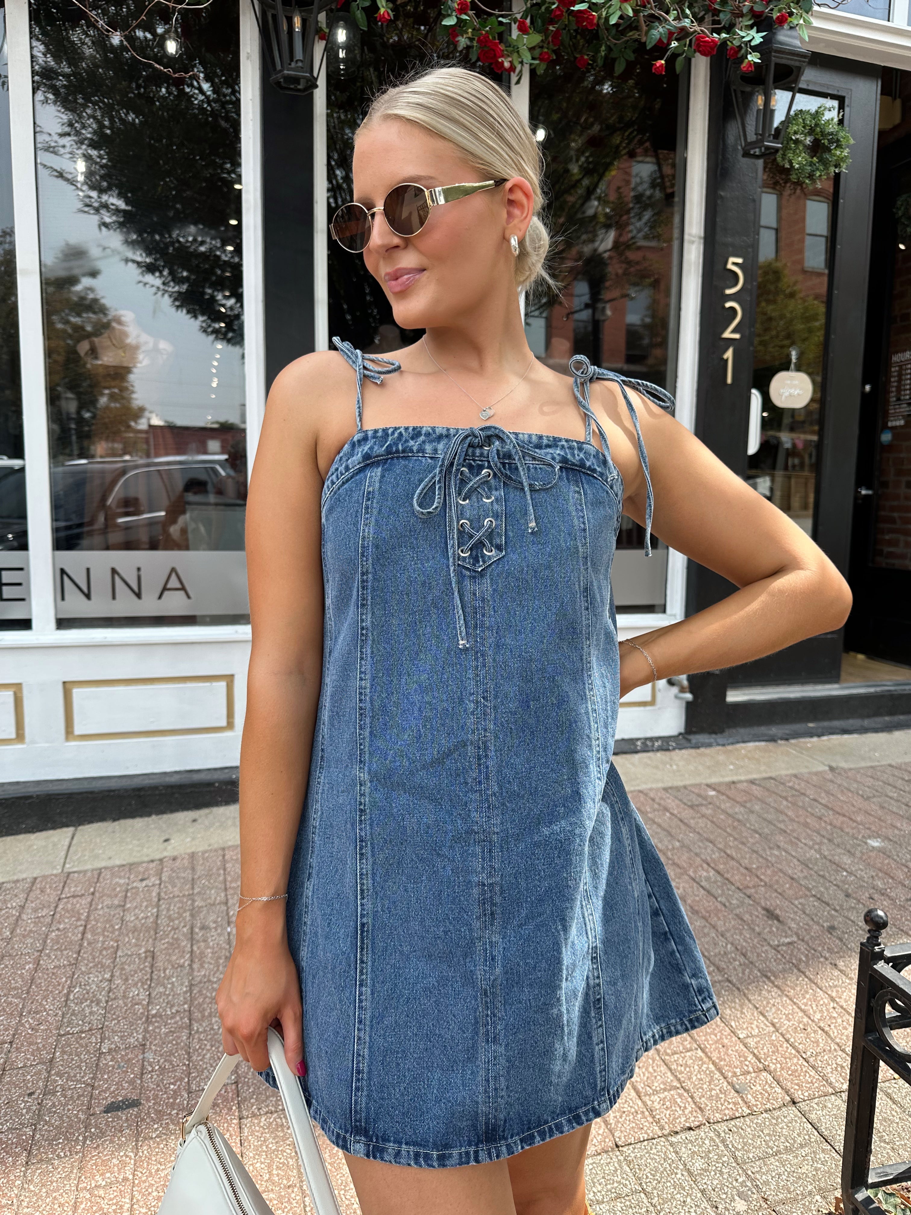 Woman wearing dark wash denim mini dress with lace up neckline detail.