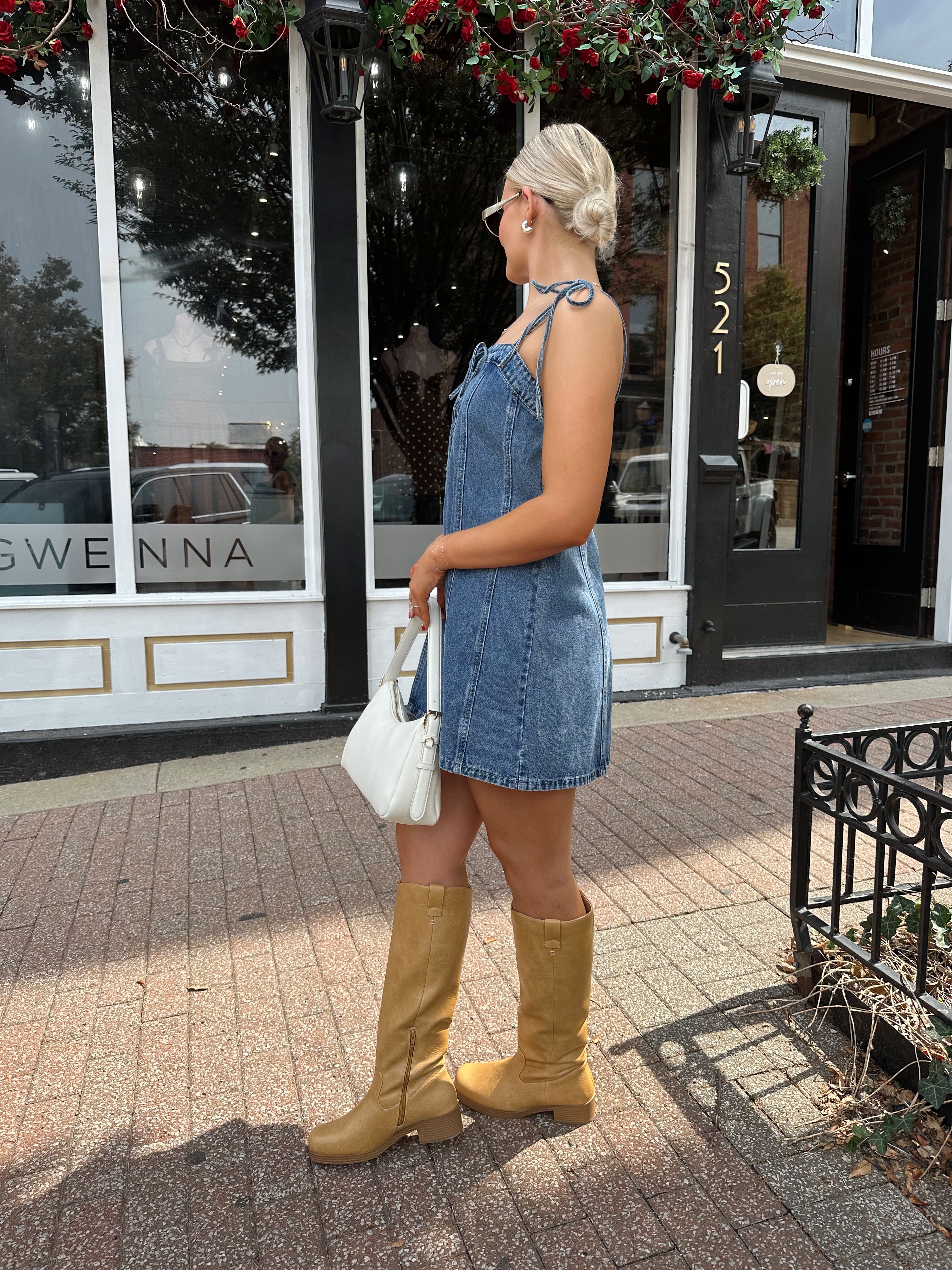 Woman wearing dark wash denim mini dress with lace up neckline detail.