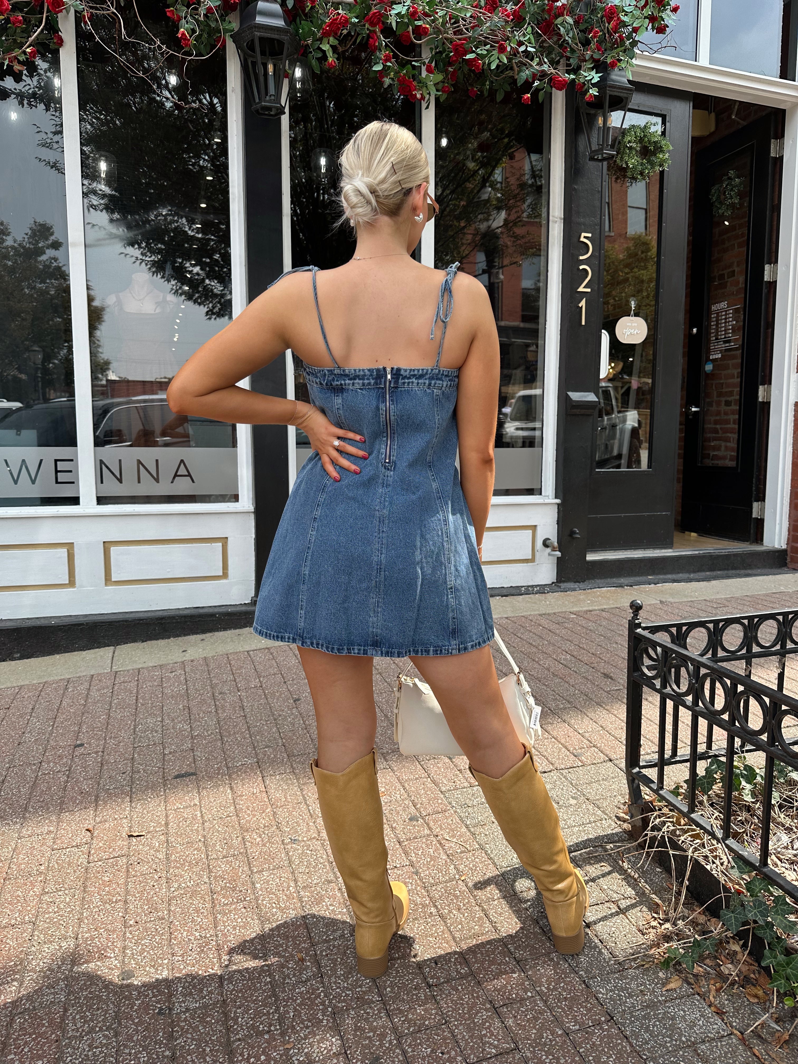 Woman wearing dark wash denim mini dress with lace up neckline detail.