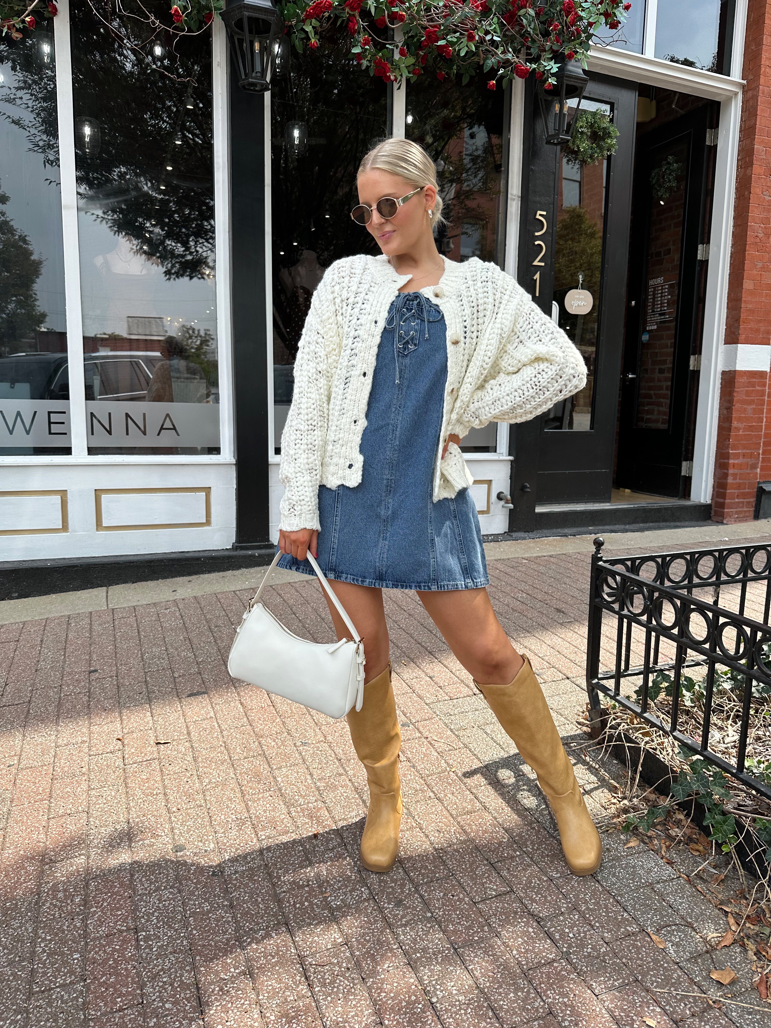 Woman wearing dark wash denim mini dress with lace up neckline detail.
