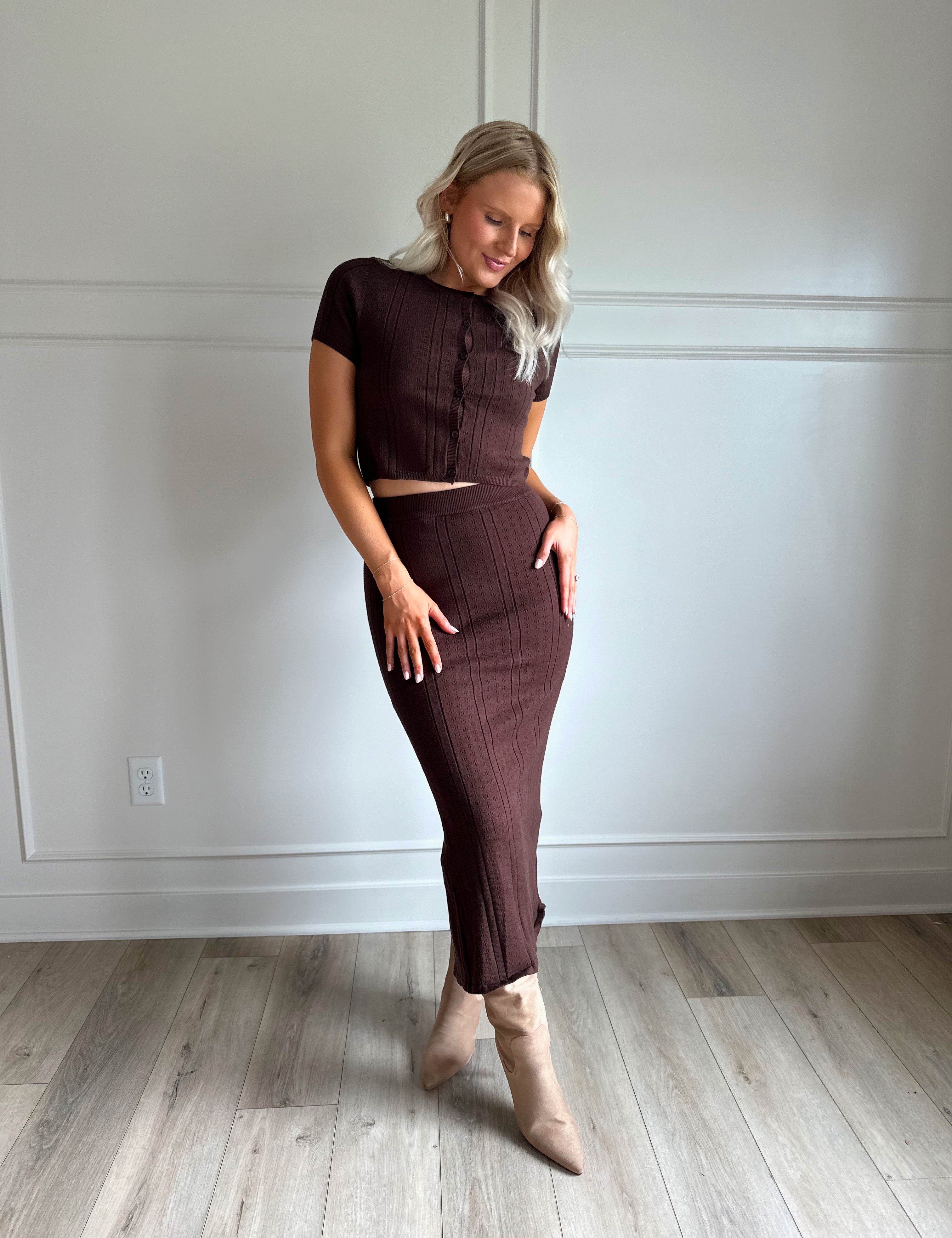 Woman with dark brown two piece knit set with short sleeve button down top, and midi length skirt with back slit.