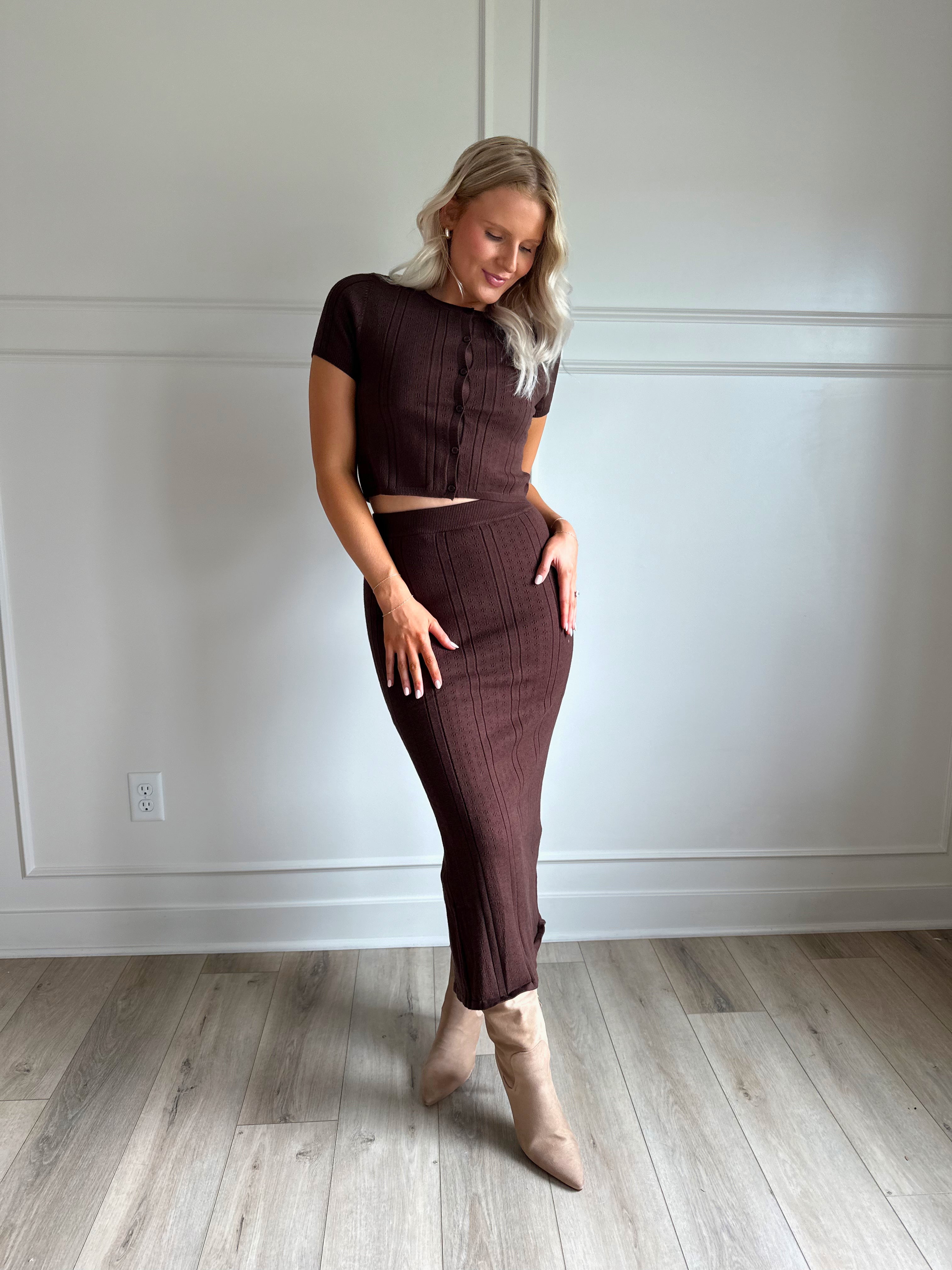 Woman with dark brown two piece knit set with short sleeve button down top, and midi length skirt with back slit.