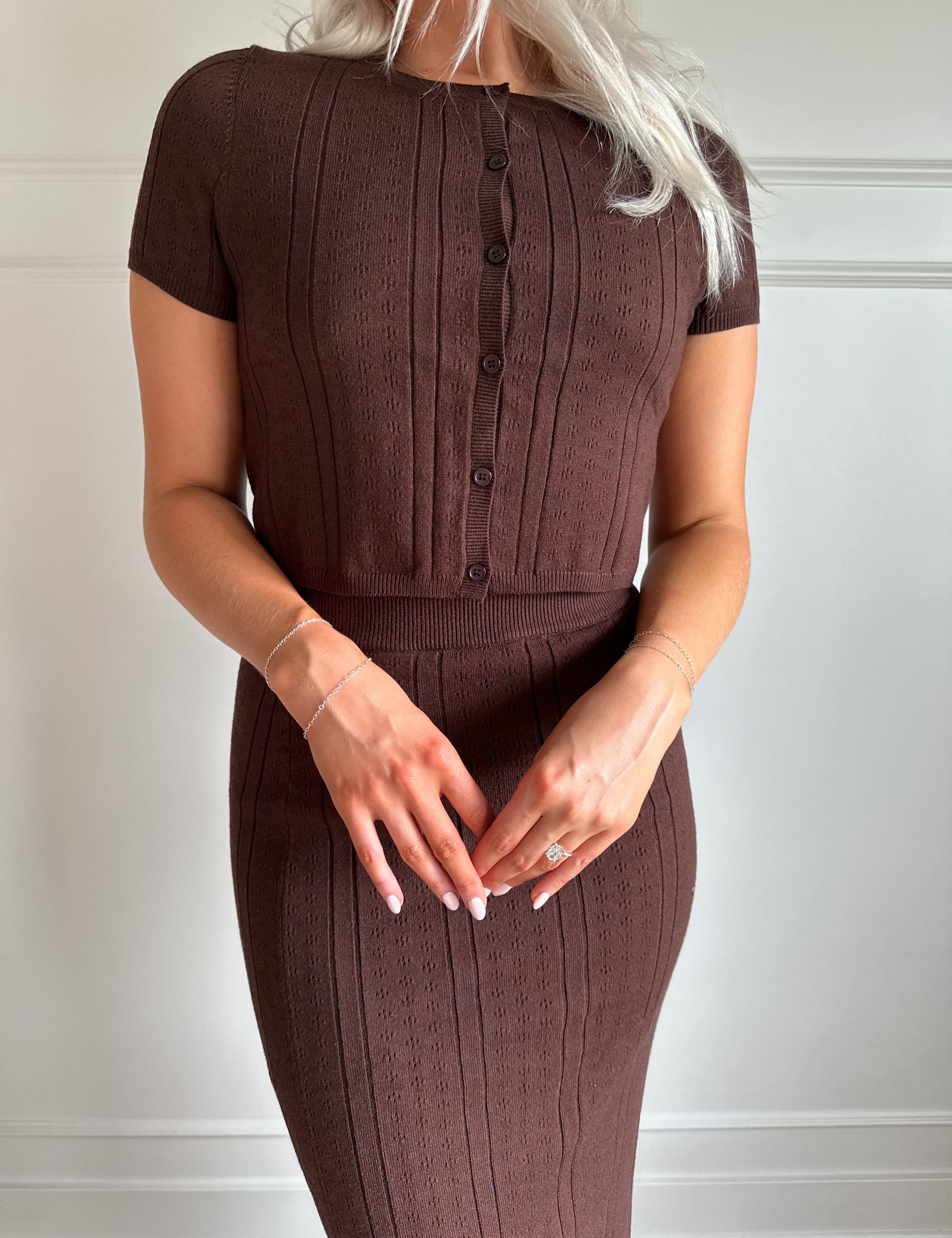 Woman with dark brown two piece knit set with short sleeve button down top, and midi length skirt with back slit.