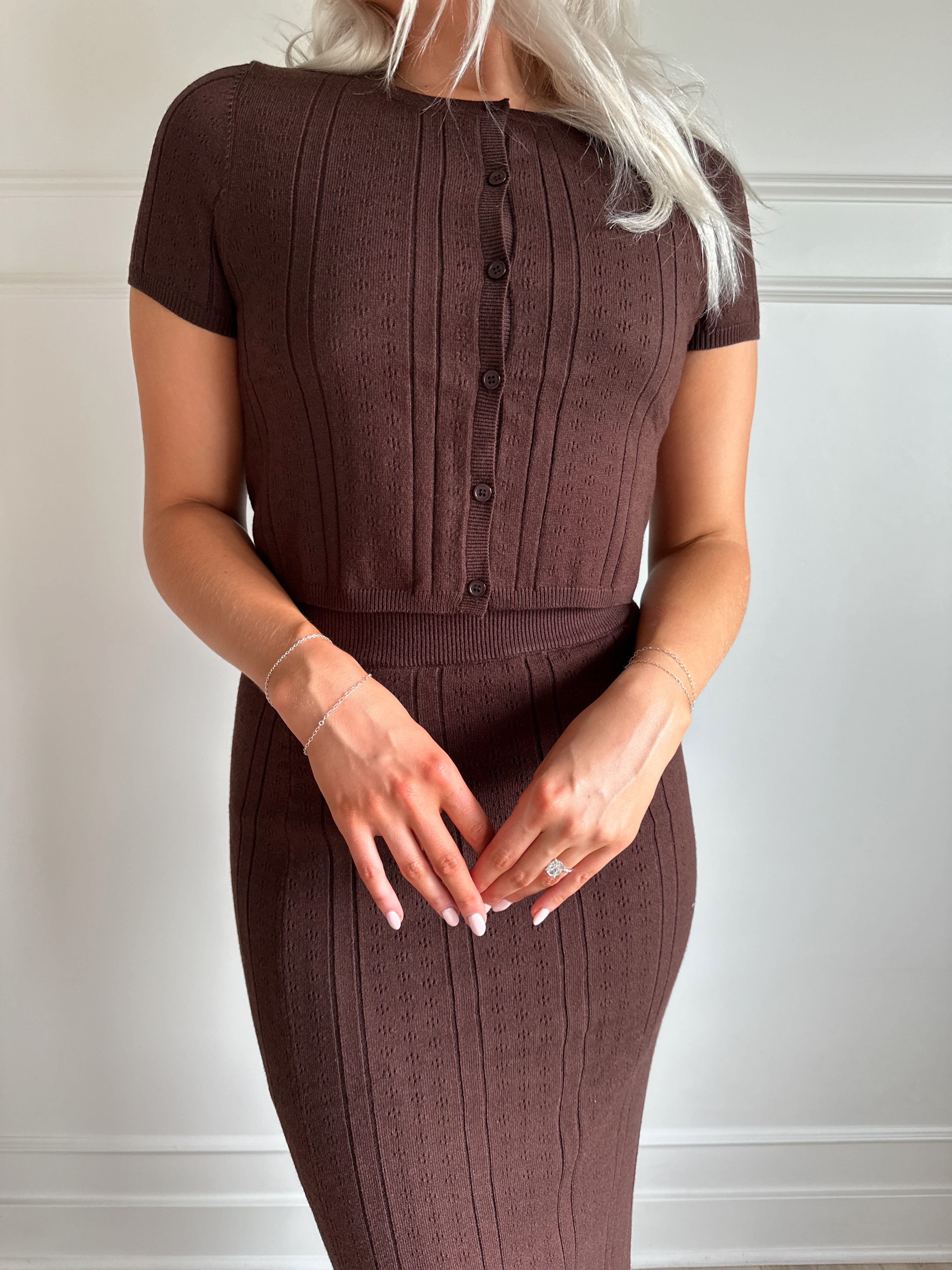Woman with dark brown two piece knit set with short sleeve button down top, and midi length skirt with back slit.