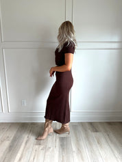  Woman with dark brown two piece knit set with short sleeve button down top, and midi length skirt with back slit.