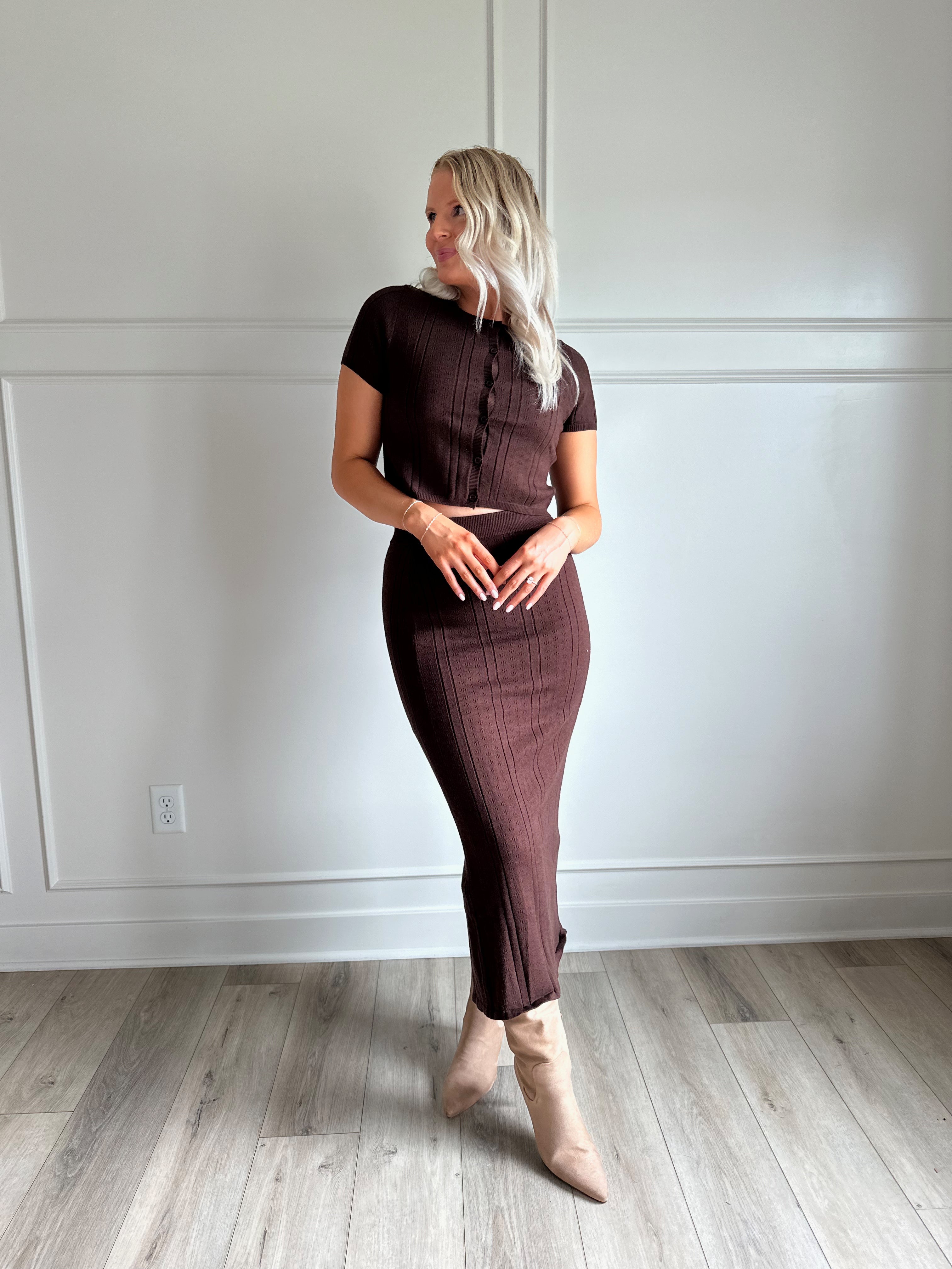 Woman with dark brown two piece knit set with short sleeve button down top, and midi length skirt with back slit.
