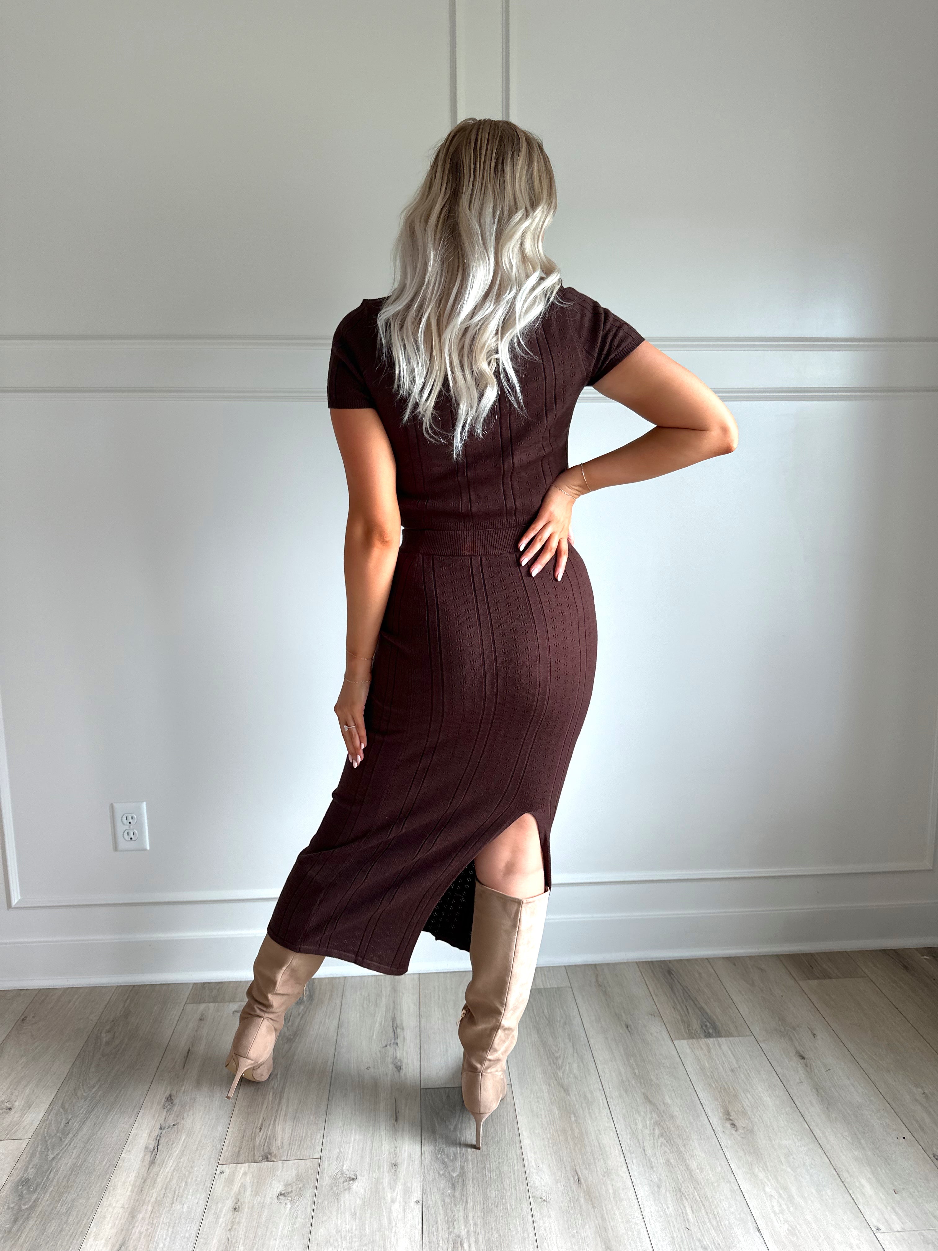Woman with dark brown two piece knit set with short sleeve button down top, and midi length skirt with back slit.
