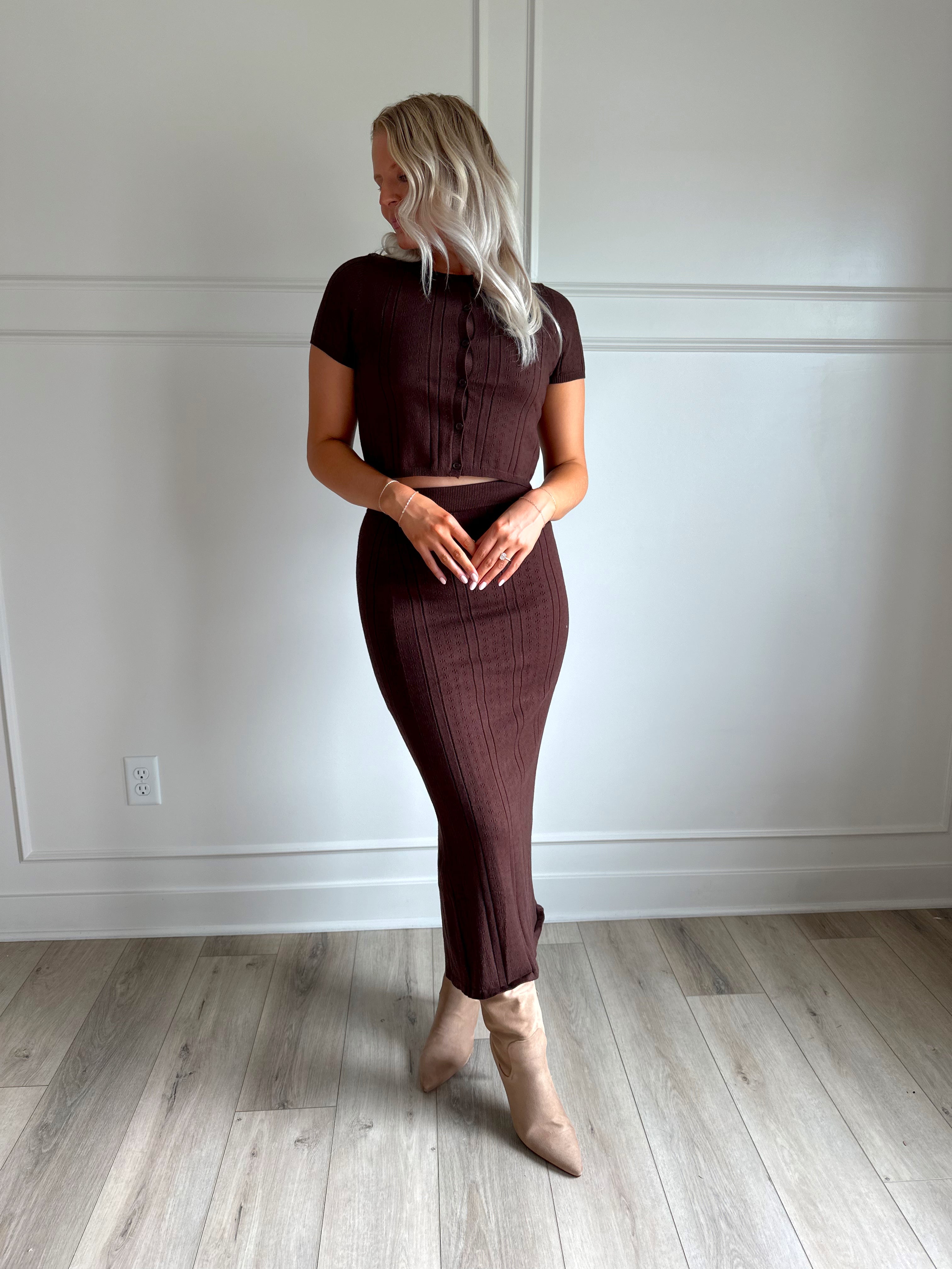 Woman with dark brown two piece knit set with short sleeve button down top, and midi length skirt with back slit.