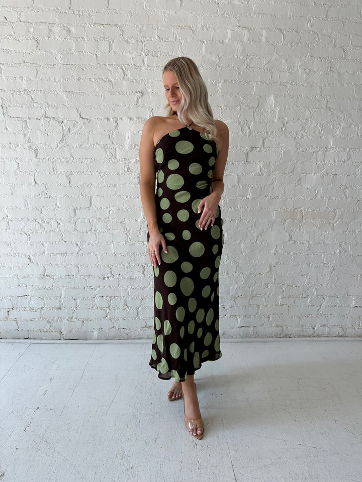 Woman wearing brown maxi dress with green polka dots, self tie halter neckline with lace up back. 