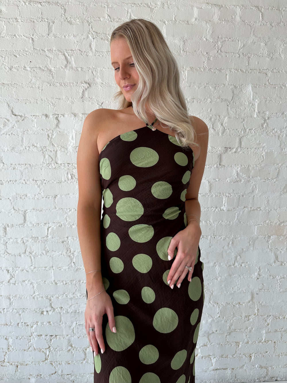 Woman wearing brown maxi dress with green polka dots, self tie halter neckline with lace up back. 