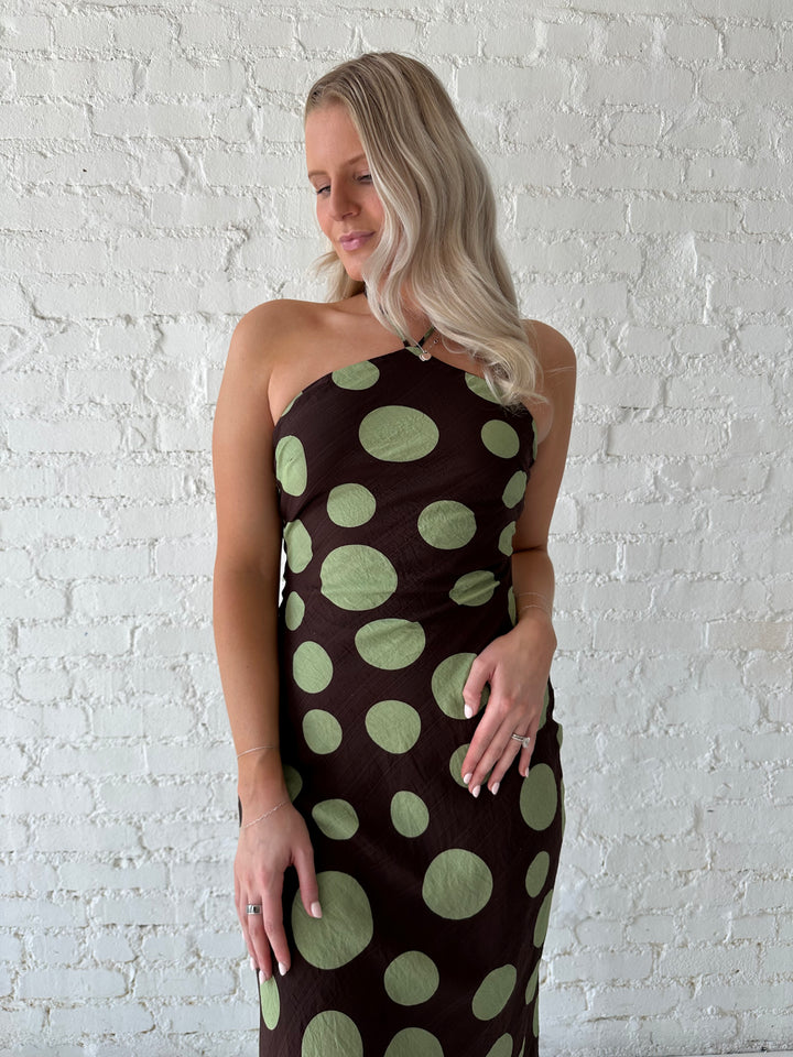 Woman wearing brown maxi dress with green polka dots, self tie halter neckline with lace up back. 