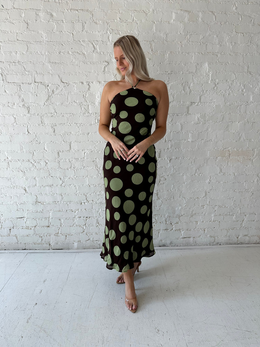 Woman wearing brown maxi dress with green polka dots, self tie halter neckline with lace up back. 