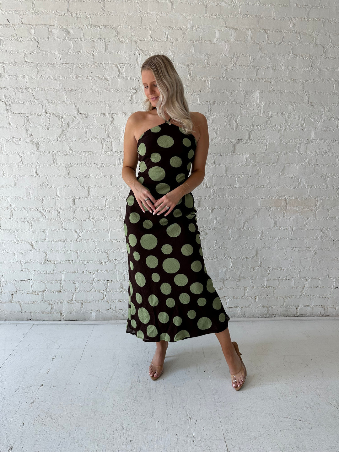 Woman wearing brown maxi dress with green polka dots, self tie halter neckline with lace up back. 