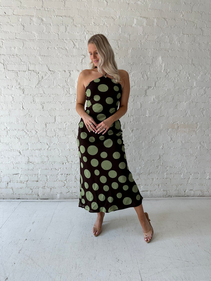 Woman wearing brown maxi dress with green polka dots, self tie halter neckline with lace up back. 