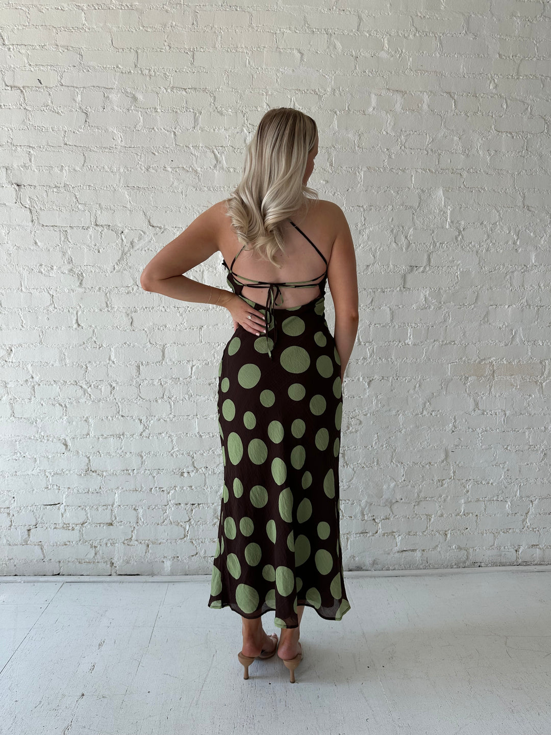 Woman wearing brown maxi dress with green polka dots, self tie halter neckline with lace up back. 