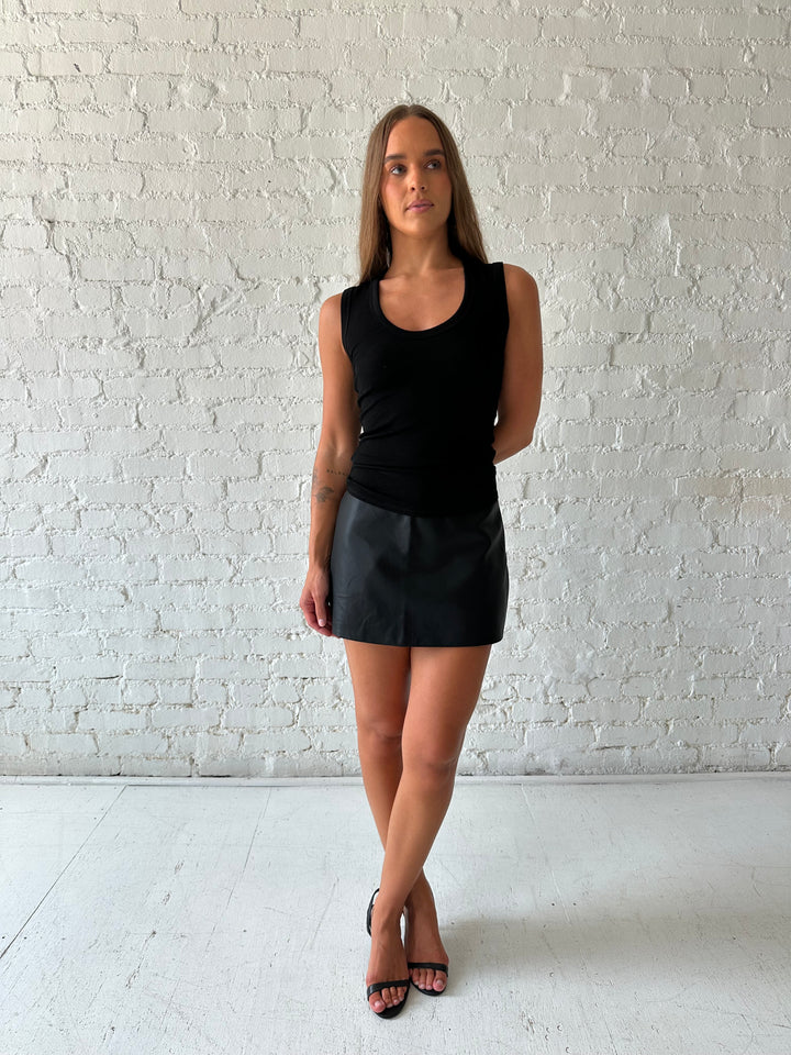 Woman wearing black leather mini skort with black ribbed tank top.