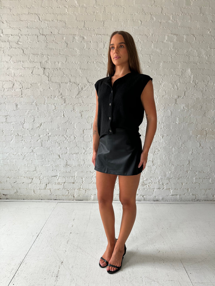 Woman wearing black leather mini skort with black knit short sleeve cardigan. 