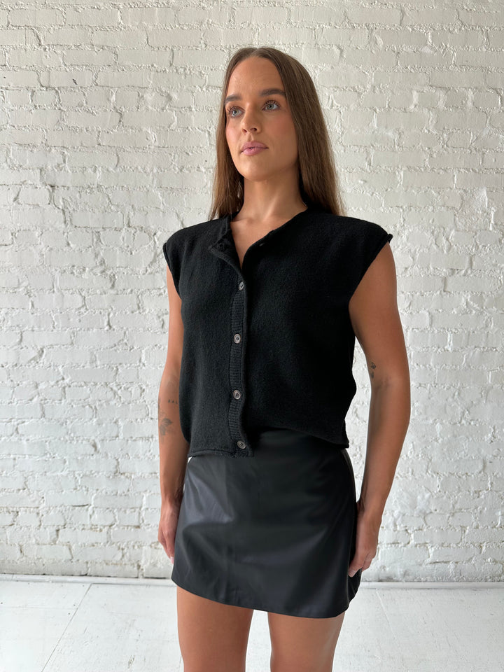 Woman wearing black leather mini skort with black knit short sleeve cardigan.