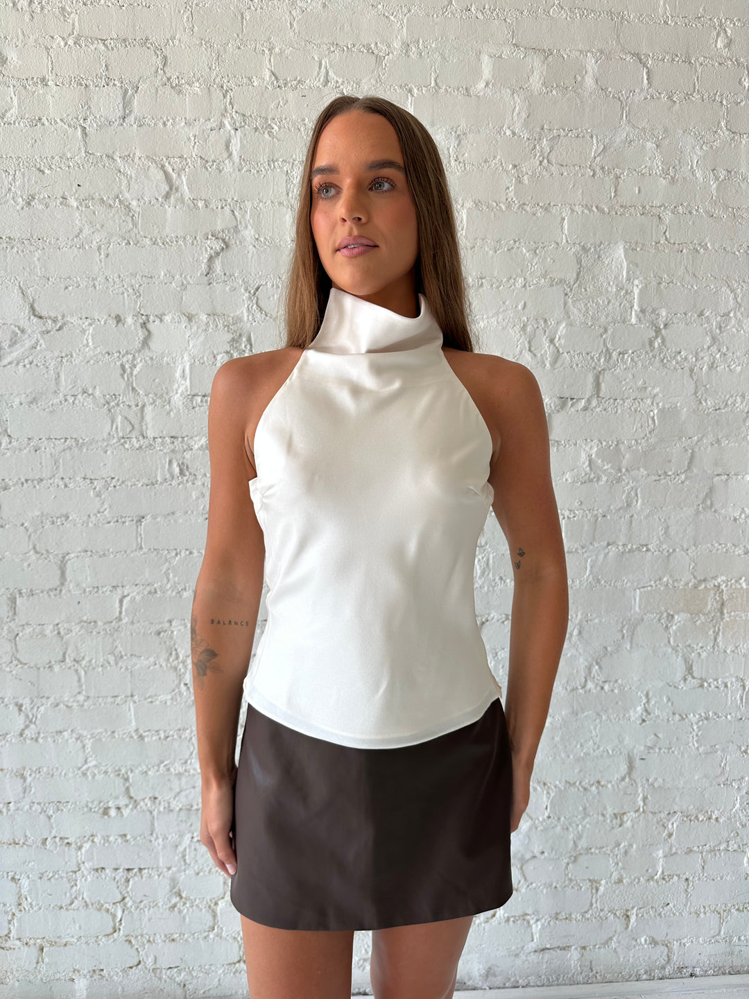 Woman wearing brown leather mini skort with cream satin cowl halter top.