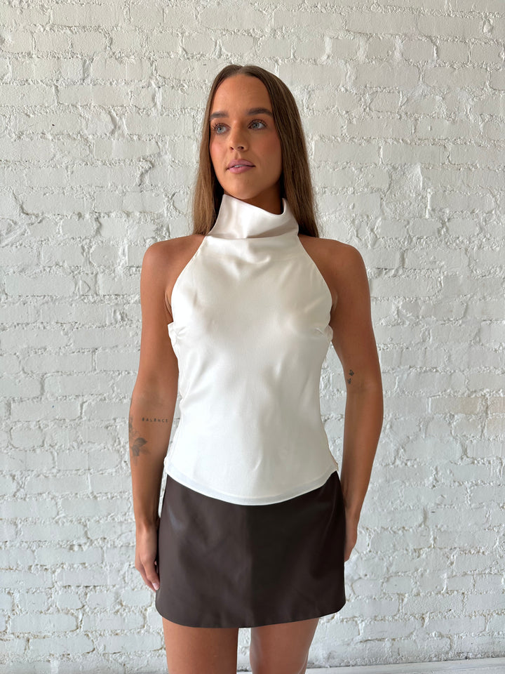 Woman wearing brown leather mini skort with cream satin cowl halter top.