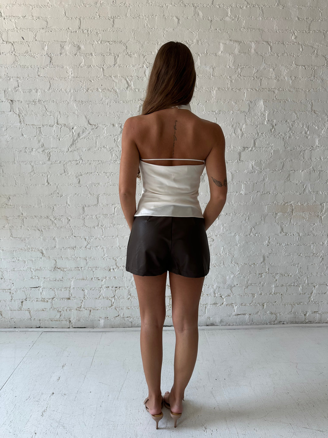 Woman wearing brown leather mini skort with cream satin cowl halter top.