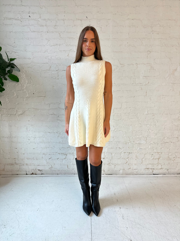 Woman wearing cream cable knit sweater mini dress with tall black knee boot. 
